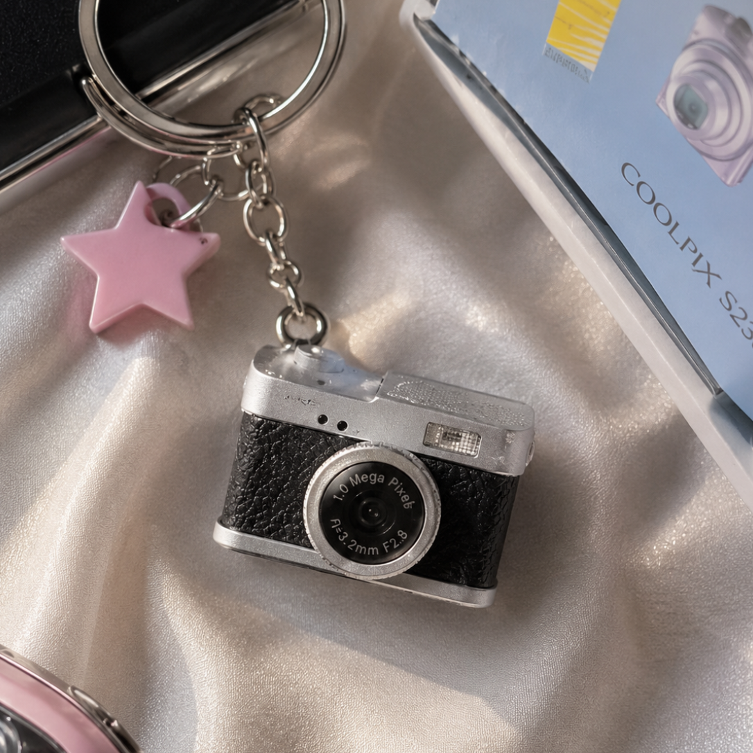 Camera-shaped keychain with pink star charm on a textured surface